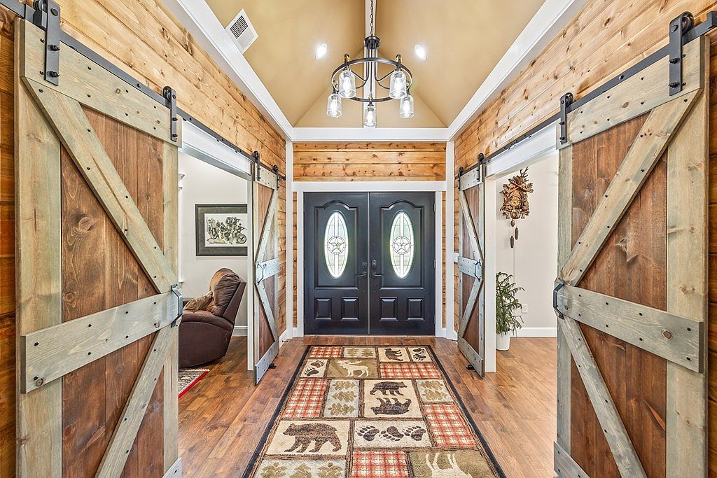 Entry foyer with custom barn-door pocket walls flanking the front door, cedar plank ceiling, and a hammered iron chandelier.